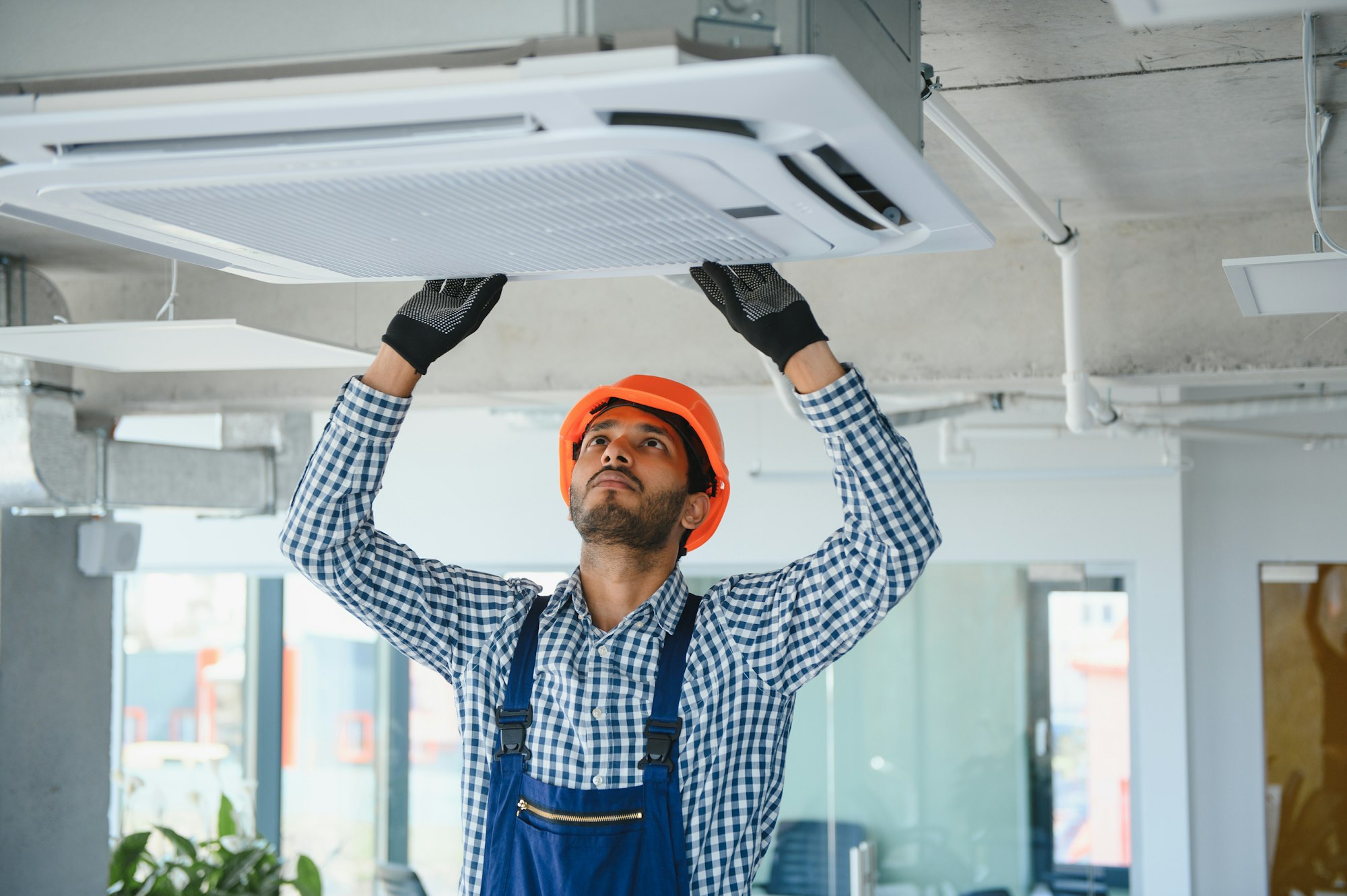 Concentrated young Indian engineer setting up air conditioner.